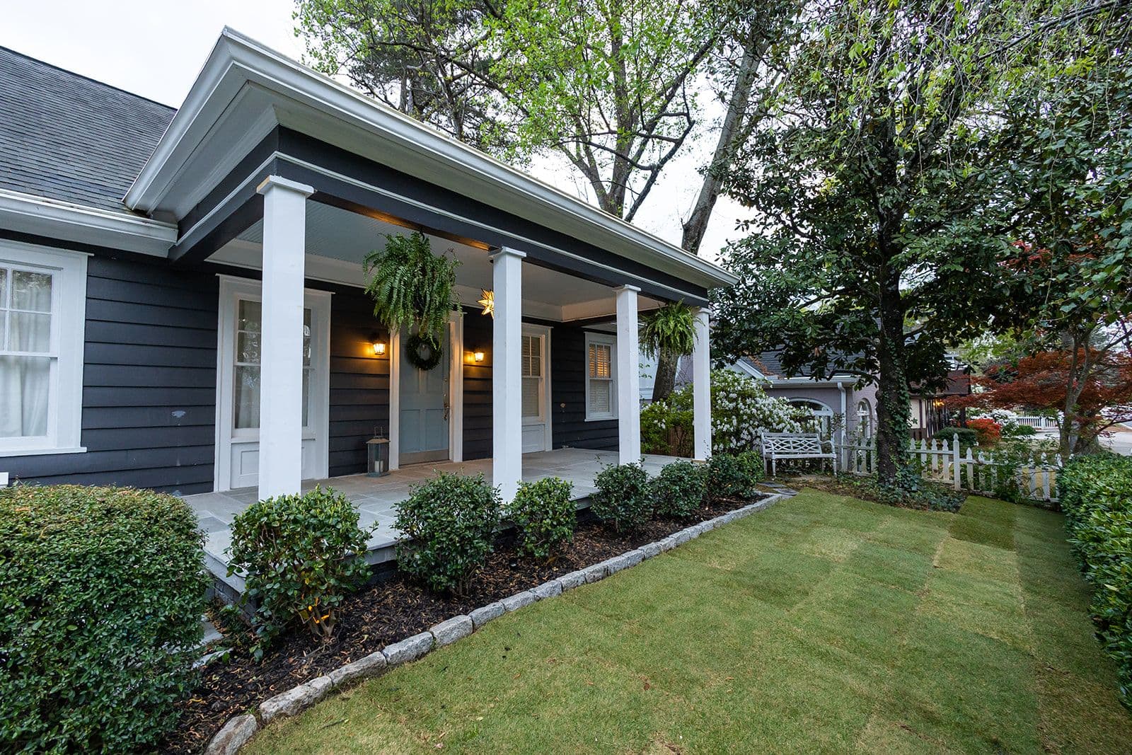 A finished front porch at dusk — lamps lit, fresh sod, planted beds
