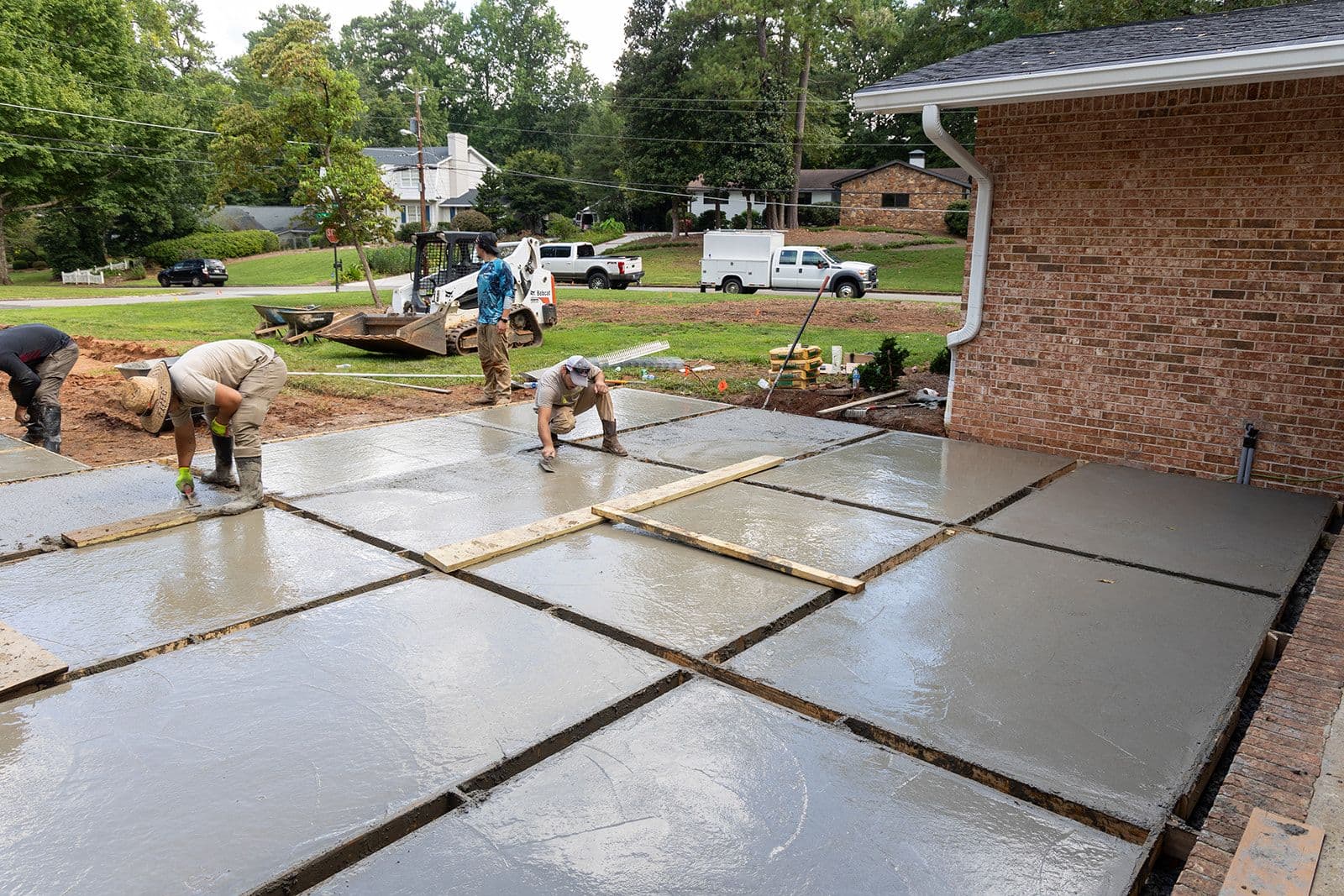 An Earthcore crew hand-floating a freshly poured concrete panel patio behind a brick home