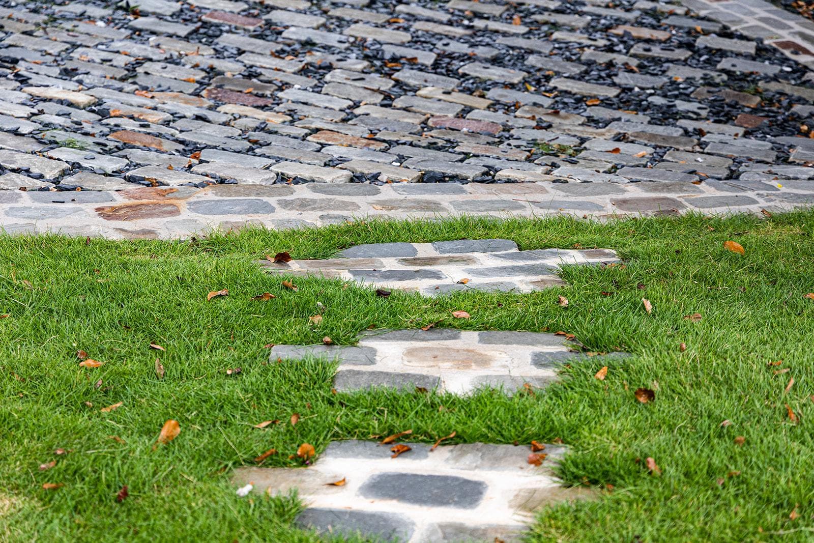 Reclaimed granite steppers set into a fresh lawn where it meets a cobblestone drive, built by Earthcore Group