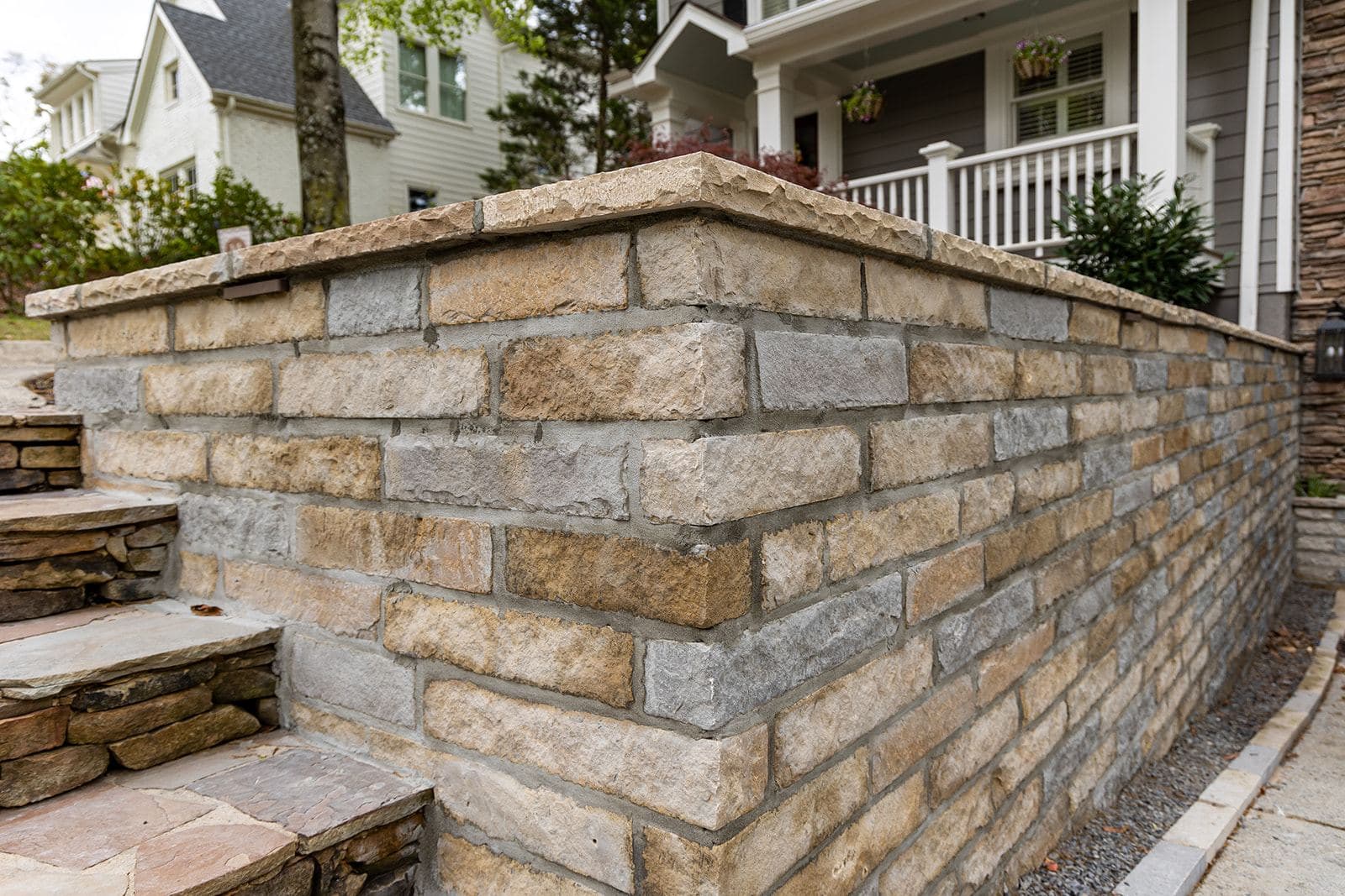 A finished dry-laid stone retaining wall with a chiseled cap and flagstone steps, fronting a Highland Avenue porch